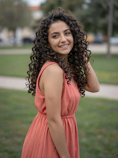Blerina, 27-year-old Albanian woman from Vlorë with curly dark hair wearing coral dress in park